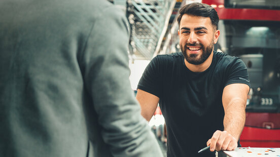 Werkstatt-Mitarbeitender lacht und steht vor Bus